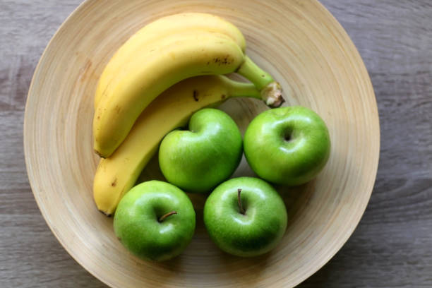 Yellow ripe banana and green apple on a gray background studio photography.