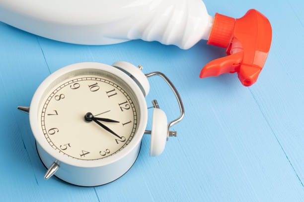 istock Spray cleaner in a white plastic container with a red dispenser and an alarm clock on a light blue wooden background 1224660460