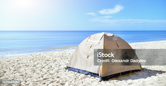 istock Sand-colored tourist tent on the seashore in the sand. Calm morning sea. camping with a tent at a lonesome beach 1224662265