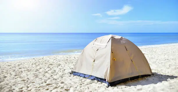 Sand-colored tourist tent on the seashore in the sand. Calm morning sea. camping with a tent at a lonesome beach.