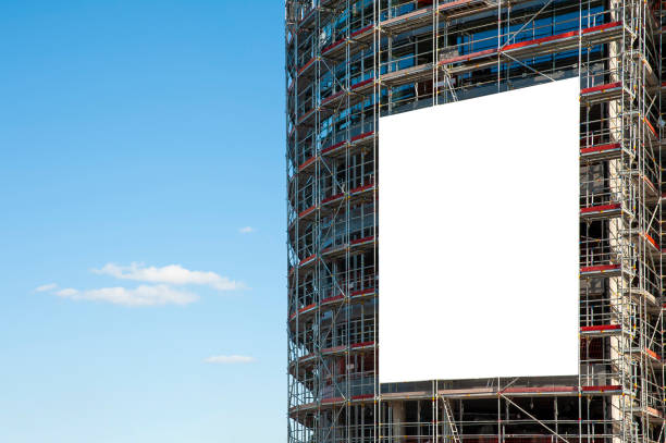 pancarta blanca en blanco para publicidad que cuelga en el andamio del edificio moderno en construcción - billboard advertisement built structure urban scene fotografías e imágenes de stock