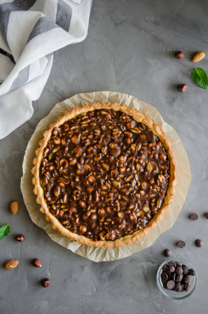 istock Tart with chocolate caramel, hazelnuts, peanuts, almonds and seed mix on a dark concrete background. Vertical orientation. Top view. 1224663688