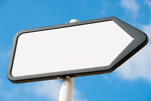 Low angle view of a plain white, blank, pointing the way, information sign post against a blue sky with clouds.