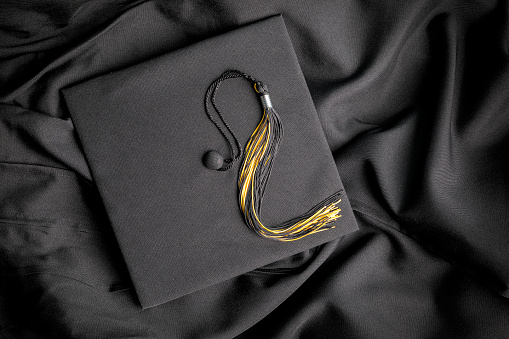 A graduation cap and tassel resting on a gown.