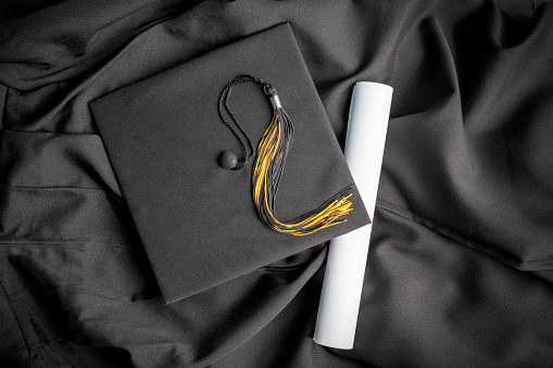 A graduation cap and tassel resting on a gown with a diploma.