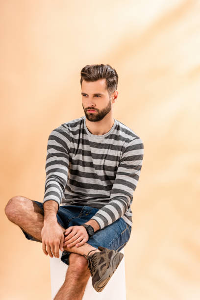 istock bearded fashionable man in striped sweatshirt sitting on white cube on beige 1224669609
