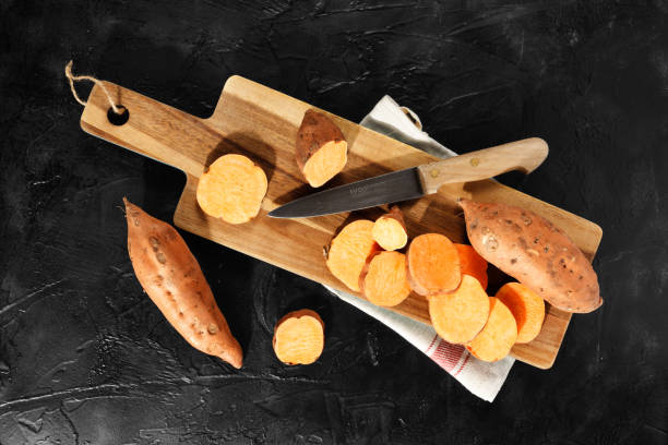 istock Raw sweet potatoes on wooden kitchen board top view. 1224671170
