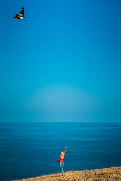 Girl on a mountainside by the sea launches a kite on a sunny day