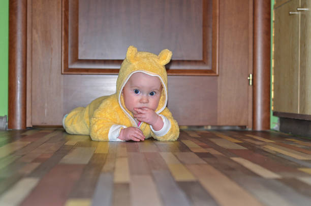 the child is 1 year old, a european crawls on the floor and looks with big eyes, sucks his hand. a child in a yellow jumpsuit. - thumb sucking cute small lying down imagens e fotografias de stock