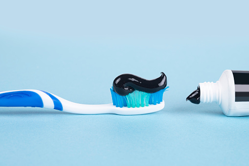 Toothbrush with black charcoal toothpaste on blue background
