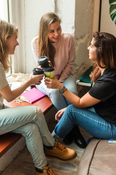 femmes modernes appréciant la rupture de café ensemble tout en ayant l’amusement et rassemblant dans le café - coffee shop coffee break coffee cup holding photos et images de collection