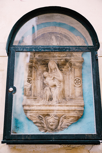 Architectural detail - a bas-relief sculpture of the Virgin Mary with baby Jesus. Venice, Italy. The bas-relief is decorated with a frame in the form of columns and an arch from above