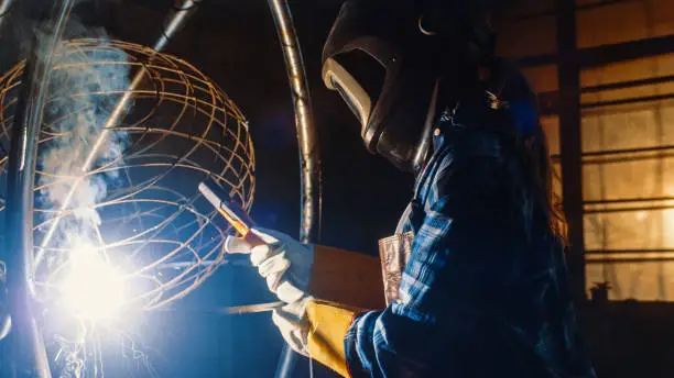Talented Emerging Female Artist is Welding an Abstract, Brutal Metal Sculpture that Reflects the Present Moment. Beautiful Tomboy Fabricator in Checkered Shirt Creating Modern Steel Art.