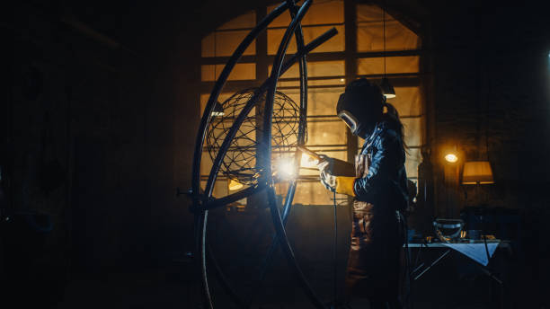 talented emerging female artist is welding an abstract, brutal metal sculpture that reflects the present moment. beautiful tomboy fabricator in checkered shirt creating modern steel art. - sculpture art abstract white imagens e fotografias de stock