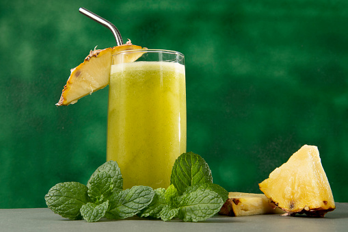 Pineapple juice in a glass and pieces of fresh pineapple on a natural wooden background. summer. fruits.