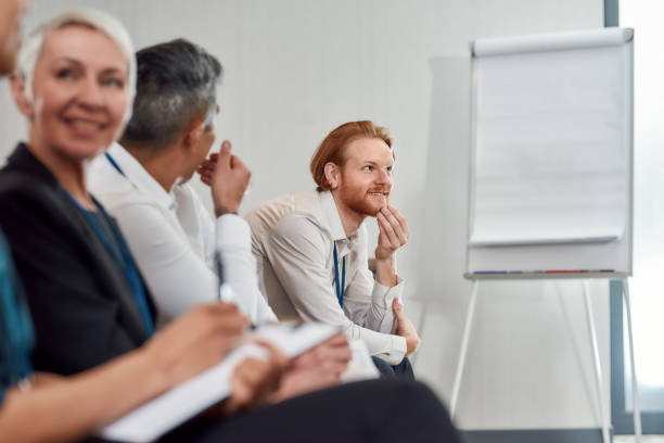 istock A world for learners. Cheerful man smiling while sitting with colleagues in a row and listening to presentation at conference hall 1224687181