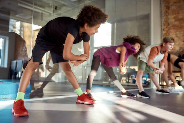 begleiten sie uns, um ergebnisse zu sehen. porträt eines jungen, der beim aufwärmen lächelt, zusammen mit anderen kindern im fitnessstudio trainiert. sport, gesunder lebensstil, aktives kindheitskonzept - warming up fotos stock-fotos und bilder