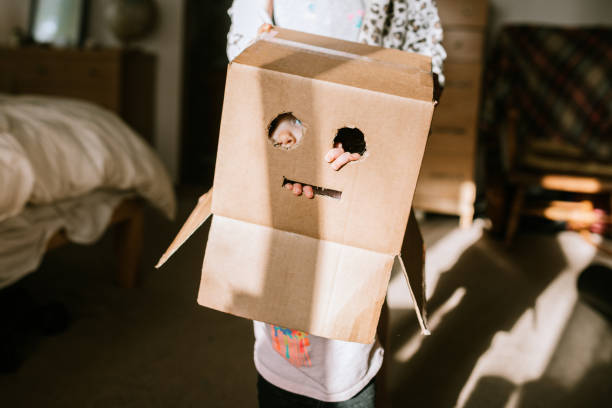 A little girl peeks through the eye holes cut in a cardboard box resembling a robot mask.  Simple and creative fun while at home.