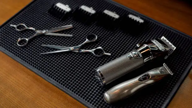 Photo of Scissors, electric hair trimmers and four different nozzles lying on a rubber mat in the barbershop. Professional barber tool kit