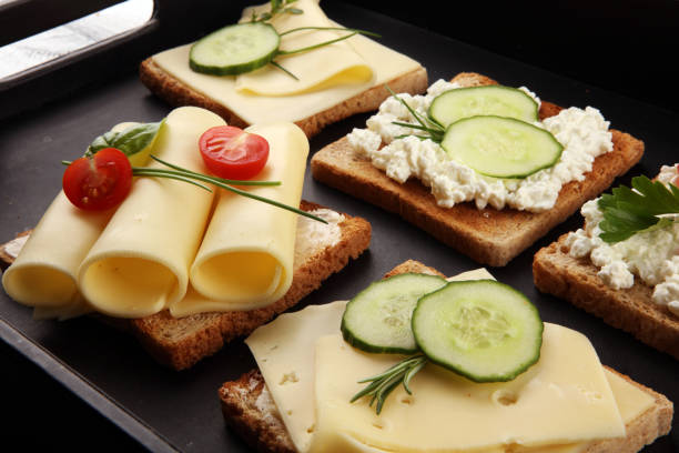 rolled slices of golden gouda cheese or cream cheese on a sandwich garnished with sliced cucumber and herbs. bread or toast with cheese for breakfast