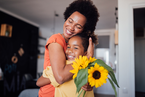 Little African American girl gifting her mother flowers for Mother's Day, making her feel special