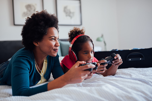 Young little African American girl with her African American mother spending some quality time together at home playing video games, competing against each other and having fun