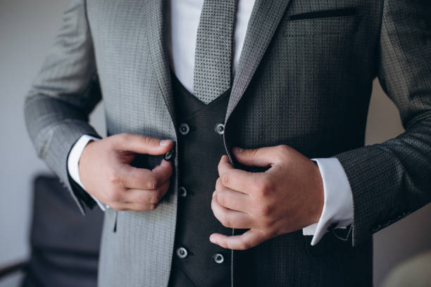 istock Young handsome stylish man dressed in modern formal clothes buttoning jacket. Close up of hands of guy in gray jacket, violet shirt. Person ready for wedding celebration or graduation. 1224708707