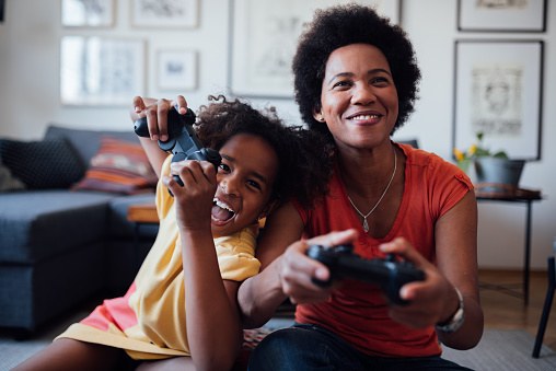 Young little African American girl with her African American mother spending some quality time together at home playing video games and having fun
