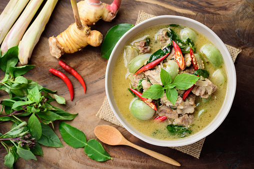Thai food, Green curry with pork (Kang Keaw Wan) in a bowl with ingredients on wooden background, Top view