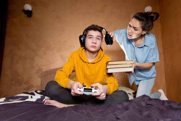 The older sister scolds her brother, who is passionate about computer games. The older sister scolds her brother, who is passionate about computer games. She is trying to convey a thought to him while he is busy playing mom and sister stock pictures, royalty-free photos & images