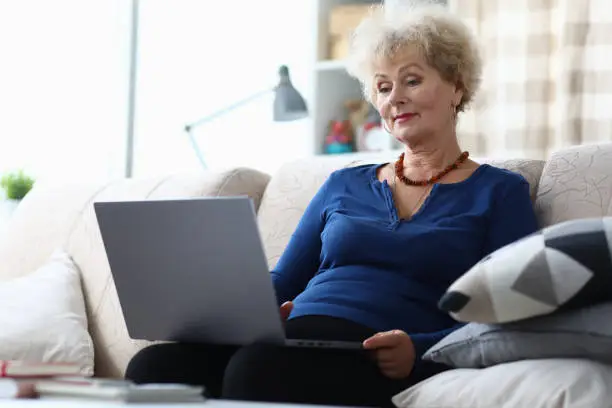 Photo of Elderly woman sitting with laptop on her lap home