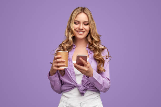 Cheerful woman with drink to go using smartphone