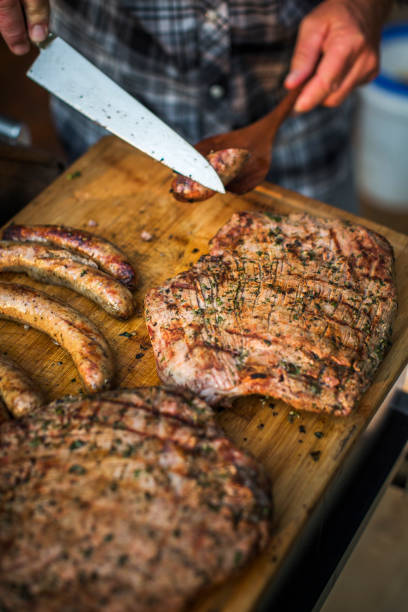 un hombre corta salchichas por encima de una tabla de cortar llena de filete de flanco y mocosos - salt sausage fire flame fotografías e imágenes de stock