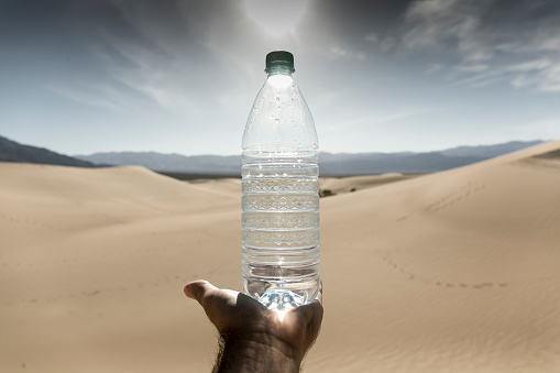 A plastic bottom of water sits on a palm in Death Valley, California