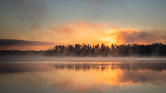 Dawn landscape at Lake Ontelaunee over a forested shore with fog at the water's surface