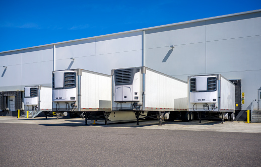 Industrial grade refrigerator semi trailers with reefer units on the front wall and without semi trucks standing at warehouse dock gates loading chilled and frozen cargo for next freight delivery