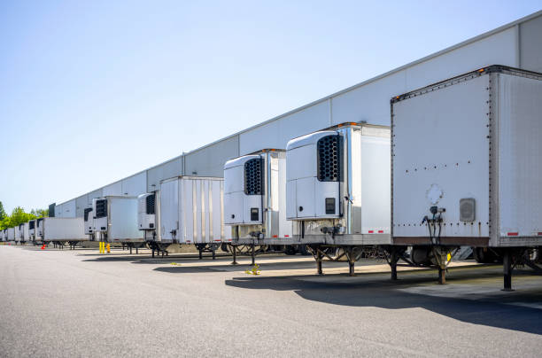 Different semi trailers without semi trucks standing at long warehouse dock gates for loading cargo for the next delivery Industrial grade refrigerator and dry van semi trailers with reefer units on the front wall and without it standing at warehouse dock gates loading commercial cargo for next freight delivery cold storage stock pictures, royalty-free photos & images