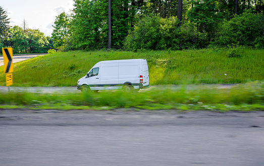 Commercial efficient eco-friendly transportation compact mini van for small business and local deliveries running on the highway entrance with green grass and trees on the hills