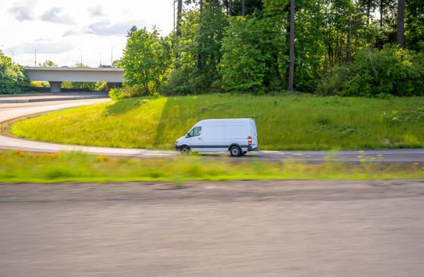 丘の上の木々や草で高速道路の入り口を回すコンパクトな白い商業貨物ミニバン - car delivering white mini van ストックフォトと画像