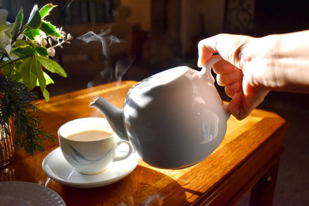 손 주전자를 들고, 태양에서 밝은 빛과 나무 테이블 배경에 연기와 컵에 뜨거운 차를 붓고, 오후에 전통적인 영어 차. - drinking tea cup drink 뉴스 사진 이미지