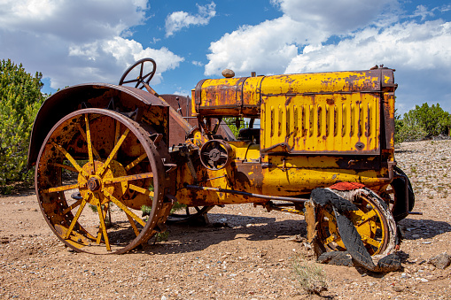 Rusted abandoned yellow vintage tractor in the desert against a cloudy sky on a sunny day