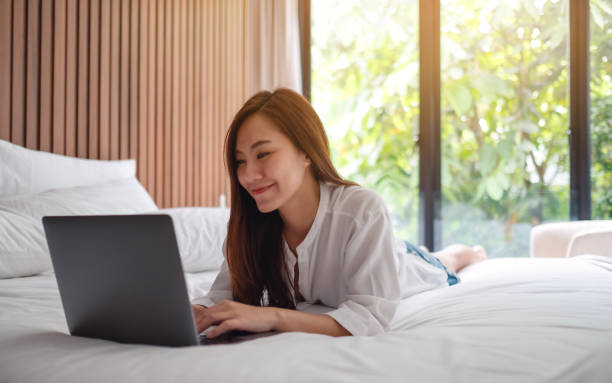 istock woman using and working on laptop computer while lying down on a white cozy bed at home 1224740712