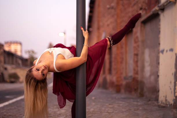 Blonde young pretty girl dancer perform in empty street leaning on pole