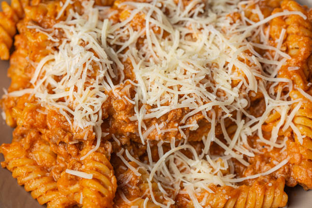Bolognese pasta served on a brown plate with grated cheese close up still