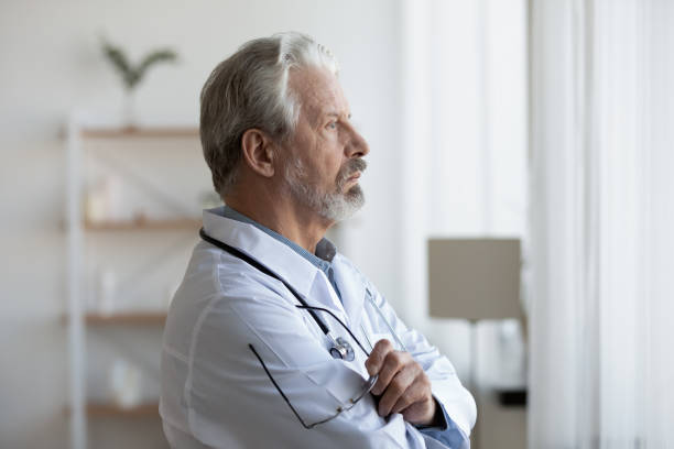 istock Thoughtful serious senior doctor looking through window lost in thoughts 1224749354