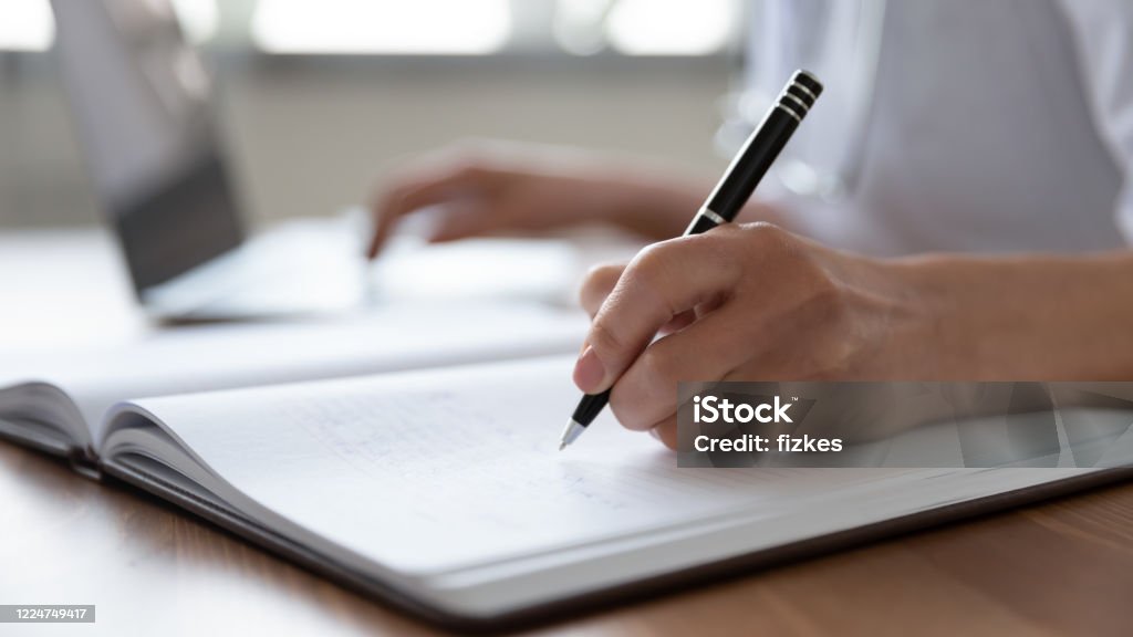 Vrouwelijke artsenhand die nota's in dagboek maakt gebruikend laptop - Royalty-free Schrijven Stockfoto