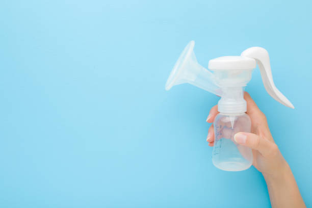 istock Young mother hand holding plastic breast pump bottle on light blue table background. Pastel color. Closeup. Preparing milk for baby feeding. Empty place for text. Top down view. 1224752129