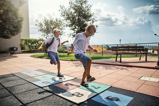 Laughing little boys playing  hopscotch in schoolyard. Nikon D850
