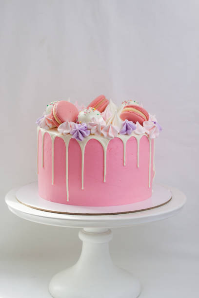 istock Tender pink cake decorated with melted white chocolate, macaroons, meringues, cake pops and candies. Plain background. 1224756368