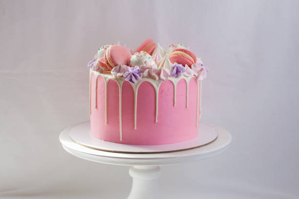 istock Tender pink cake decorated with melted white chocolate, macaroons, meringues, cake pops and candies. Plain background. 1224756375